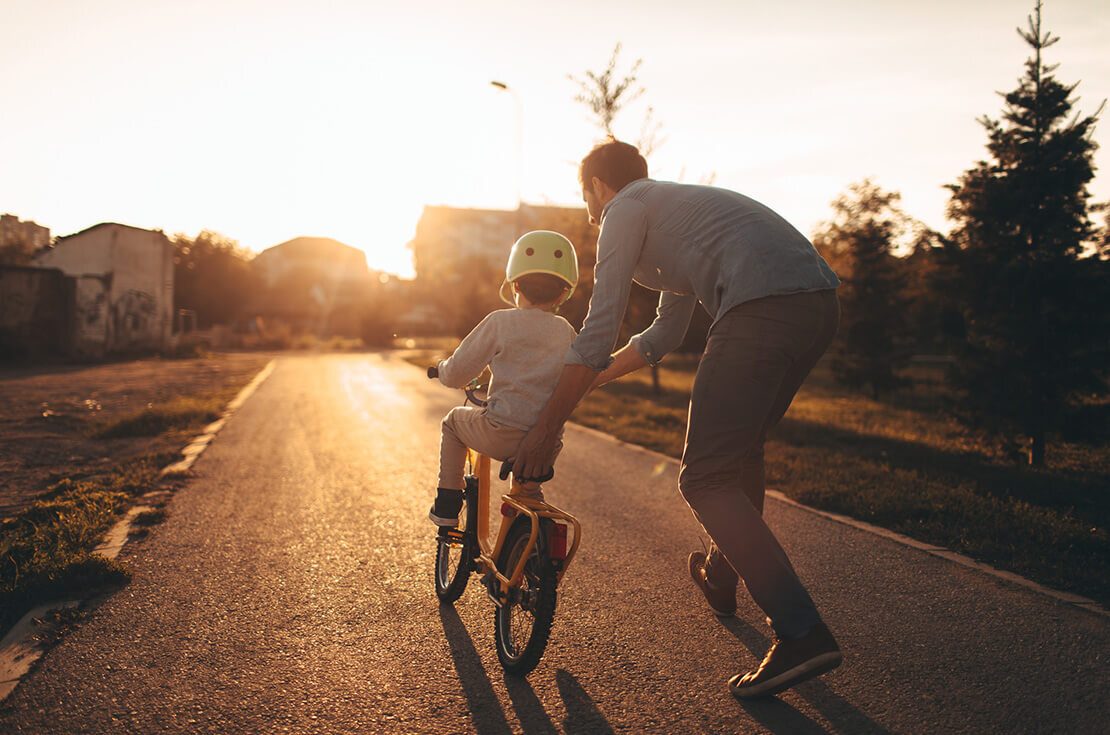 Photo of a young boy and his father on a bicycle lane, learning to ride a bike.